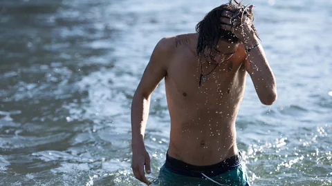 Ein Mann in Badehose steigt aus dem Wasser.