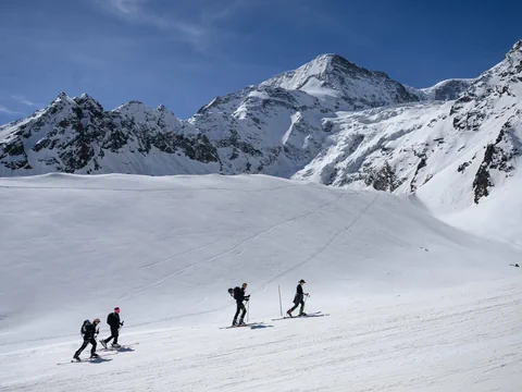 Vier Skifahrer auf schneebedecktem Berg mit blauem Himmel.