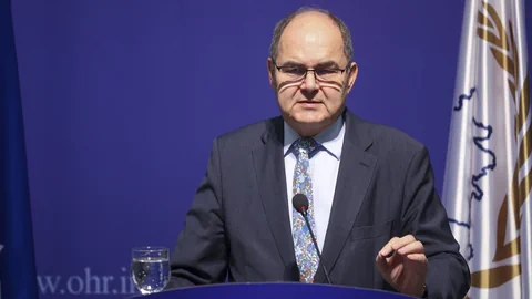 Mann im Anzug hält eine Rede vor blauem Hintergrund.