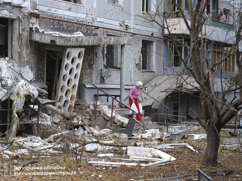 Schwer beschädigtes Haus, eine ältere Frau mit im Bild.