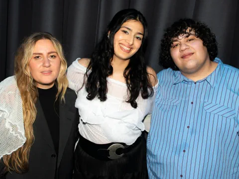 Zwei Frauen und ein Mann posieren vor einem schwarzen Vorhang