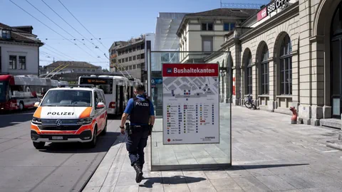 Ein Polizist geht an einer Bushaltestelle neben einem Polizeiauto und Gebäuden vorbei.