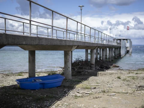 Steg führt über den Sand zum Wasser, mit einem blauen Boot im Vordergrund.