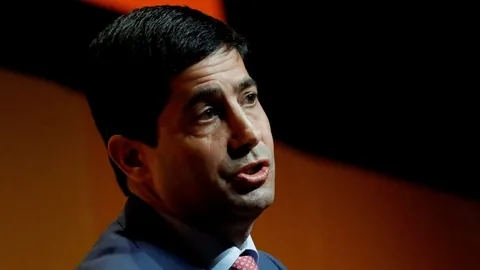 Mann in Anzug spricht, dunkler Hintergrund.