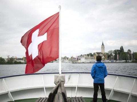 Mann in blauer Jacke steht auf einem Boot mit Schweizer Flagge.
