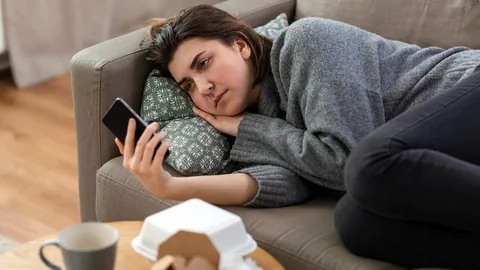 Eine junge Frau liegt auf dem Sofa und starrt in ihr Smartphone.