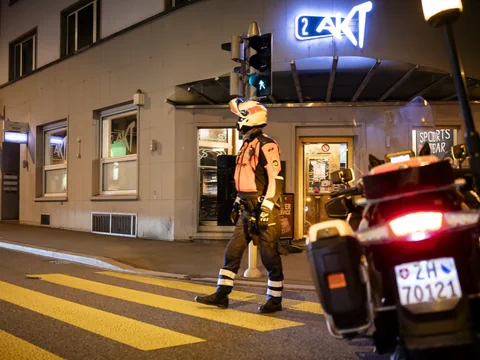 Ein Polizist mit Helm steht an einem Zebrastreifen neben einem Motorrad vor einer Bar in der Nacht.
