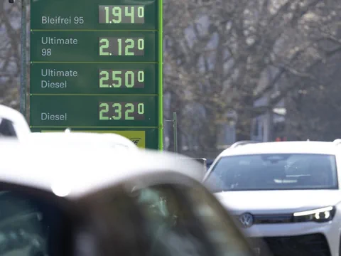 Preistafel einer Tankstelle mit Autos im Vordergrund.