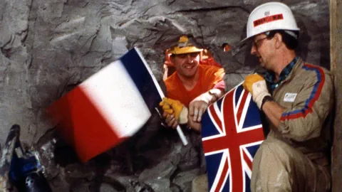 Französischer und britischer Arbeiter halten ihre Nationalflaggen in einem Tunnel.