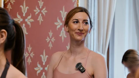 Lächelnde Frau in Trägertop in einem Raum mit verziertem Hintergrund und Vorhängen.