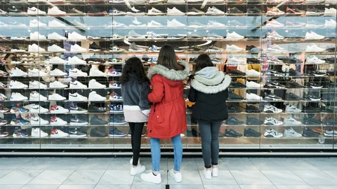 Drei Teenager stehen vor einem Schaufenster voller Sneakers