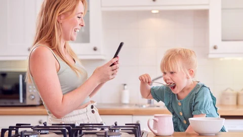 Eine Mutter fotografiert mit dem Handy ihr Kind, das gerade am Müesliessen ist.