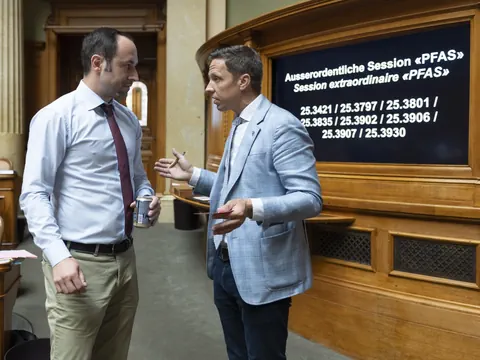 Zwei Männer in einem Gespräch vor einer Tafel mit Text im Hintergrund.