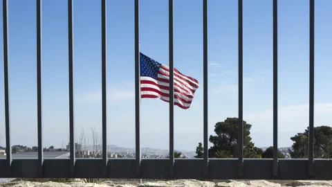US-Flagge weht hinter einem Gitter.
