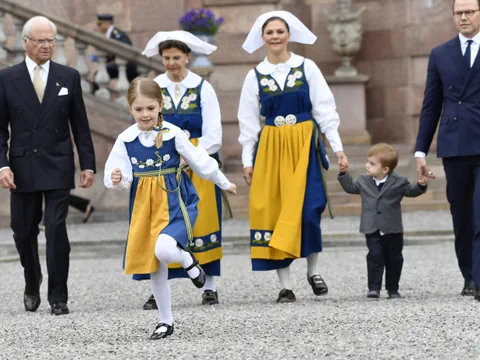 Gruppe von Menschen in traditioneller Kleidung auf einem Kiesweg.