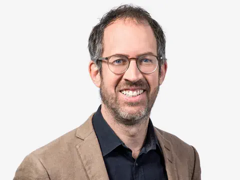 Mann mit Brille und Bart lächelnd im Anzug.