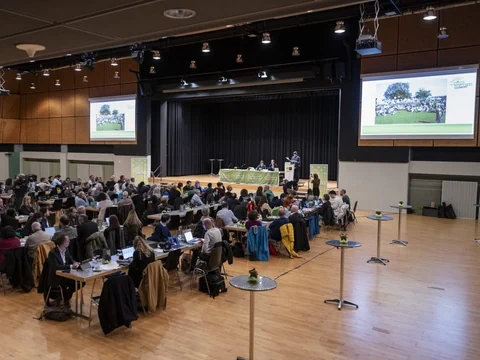 Besucher in einer Konferenzhalle mit Präsentation auf Bildschirmen.