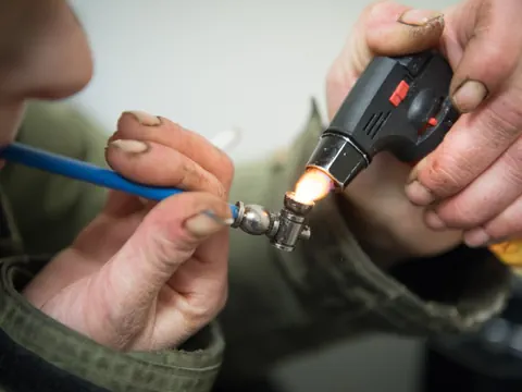 Person lötet Metallstück mit Flamme, Nahaufnahme.