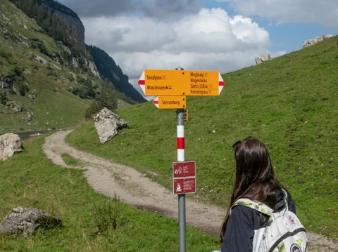 Wandererin vor Wegweiser in alpiner Landschaft.
