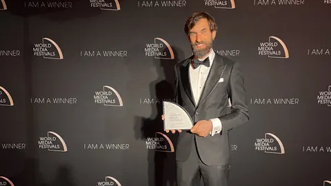 Mann in festlichem Anzug mit Award vor einer Fotowand.