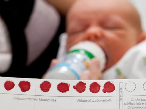 Nahaufnahme eines Babys, das aus einer Flasche trinkt, mit einer Karte im Vordergrund.