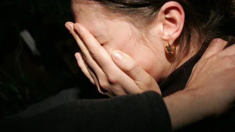 Mädchen hält sich Hand vor Gesicht, männliche Hand auf Schulter.