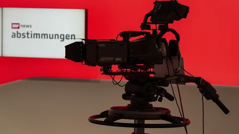 Kamera in einem Studio mit rotem Hintergrund und Bildschirm.