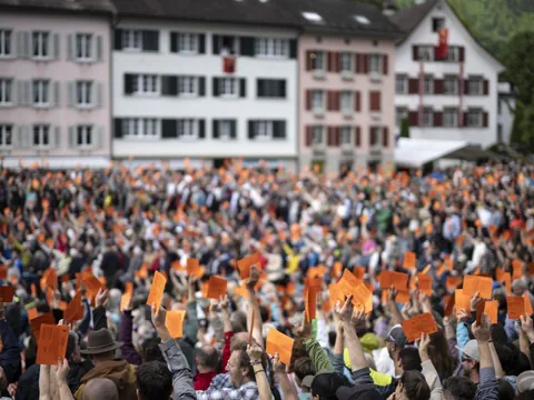 Grosse Menschenmenge hebt orange Stimmkarten vor Gebäuden hoch.