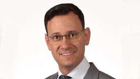 Mann mit Brille und Anzug lächelt.