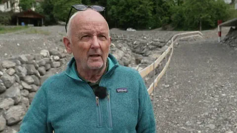 Ein Mann mit einer blauen Jacke und einer Brille auf dem Kopf auf einer steinigen Strasse.