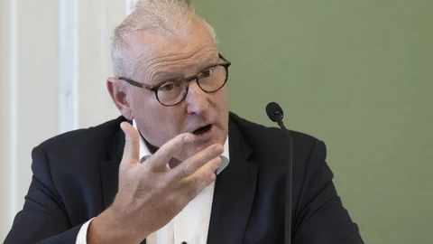 Person mit Brille und Anzug spricht in ein Mikrofon.