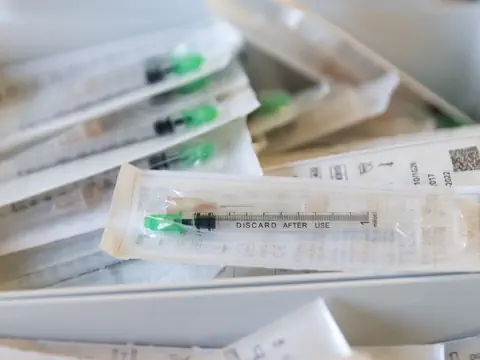 Nahaufnahme von verpackten Einwegspritzen mit grünen Kappen.
