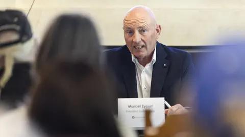 Ein Mann in einem Anzug spricht bei einem Treffen vor mehreren Personen.