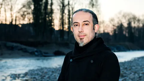 Ein Mann mit zusammengebundenem Haar uns Spitzbärtchen steht an der Aare.