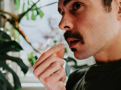 Mann mit Schnurrbart und Nasenring berührt seine Lippe.