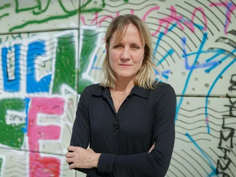 Frau vor mit Graffiti besprühten Wand, Arme verschränkt.