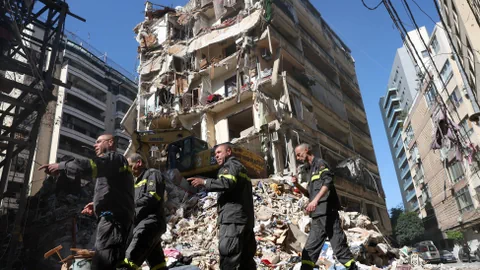 Rettungskräfte gehen vor einem zerstörten Gebäude.