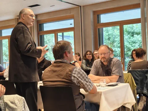 Personen bei einer Besprechung in einem Raum mit Fenstern.