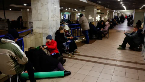 Menschen sitzen auf dem Boden und Bänken in einem U-Bahn-Tunnel.