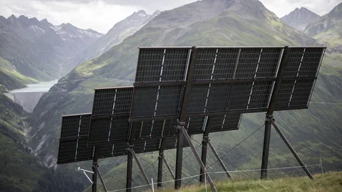 Solarmodule in bergiger Landschaft mit Tal im Hintergrund.