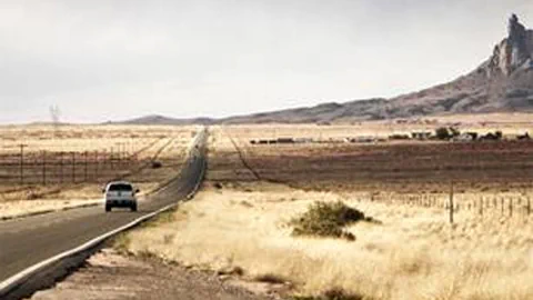 Ein Auto fährt auf einer geraden Strasse durch eine öde trockene Landschaft.
