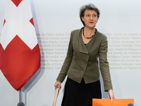 Person in Anzug mit Schweizer Flagge im Hintergrund.