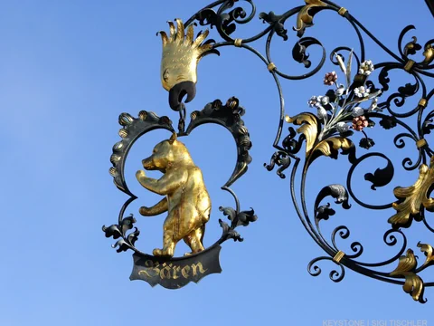 Metallschild mit goldenem Bären und filigranen Verzierungen.