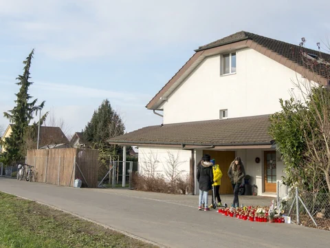 Personen versammeln sich mit Blumen und Kerzen vor einem Haus.