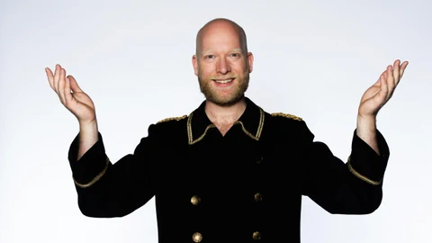 Porträt von August Schram, die Hände angehoben, mit den Handflächen gegen oben.