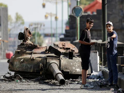 Zwei Jungen neben einem zerstörten Panzer auf der Strasse.