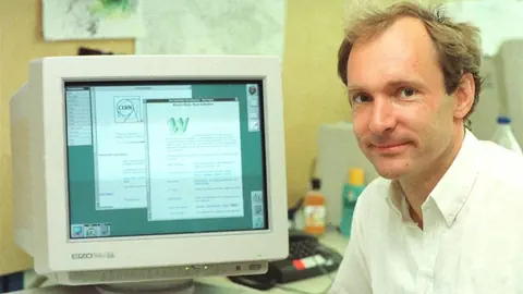 Timothy Berners-Lee neben einem Computerbildschirm mit geöffneter Webseite.