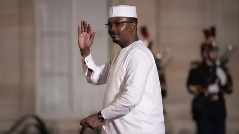 Mahamat Idriss Déby in weissem traditionellen Kleid winkt in die Kamera. 