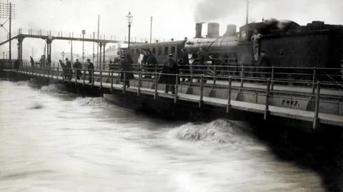 Dampfzug auf Brücke bei Hochwasser.
