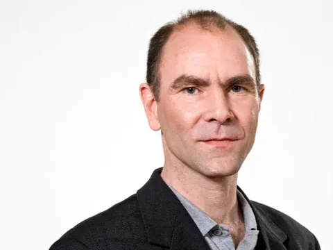 Porträt eines Mannes in schwarzem Sakko vor weissem Hintergrund.